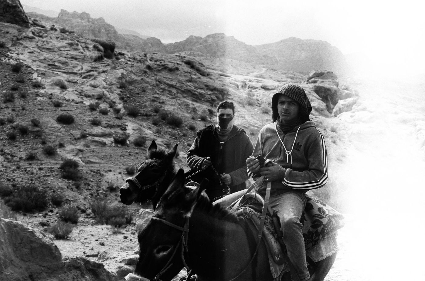Two young men on donkeys on a rocky mountain path, black and white