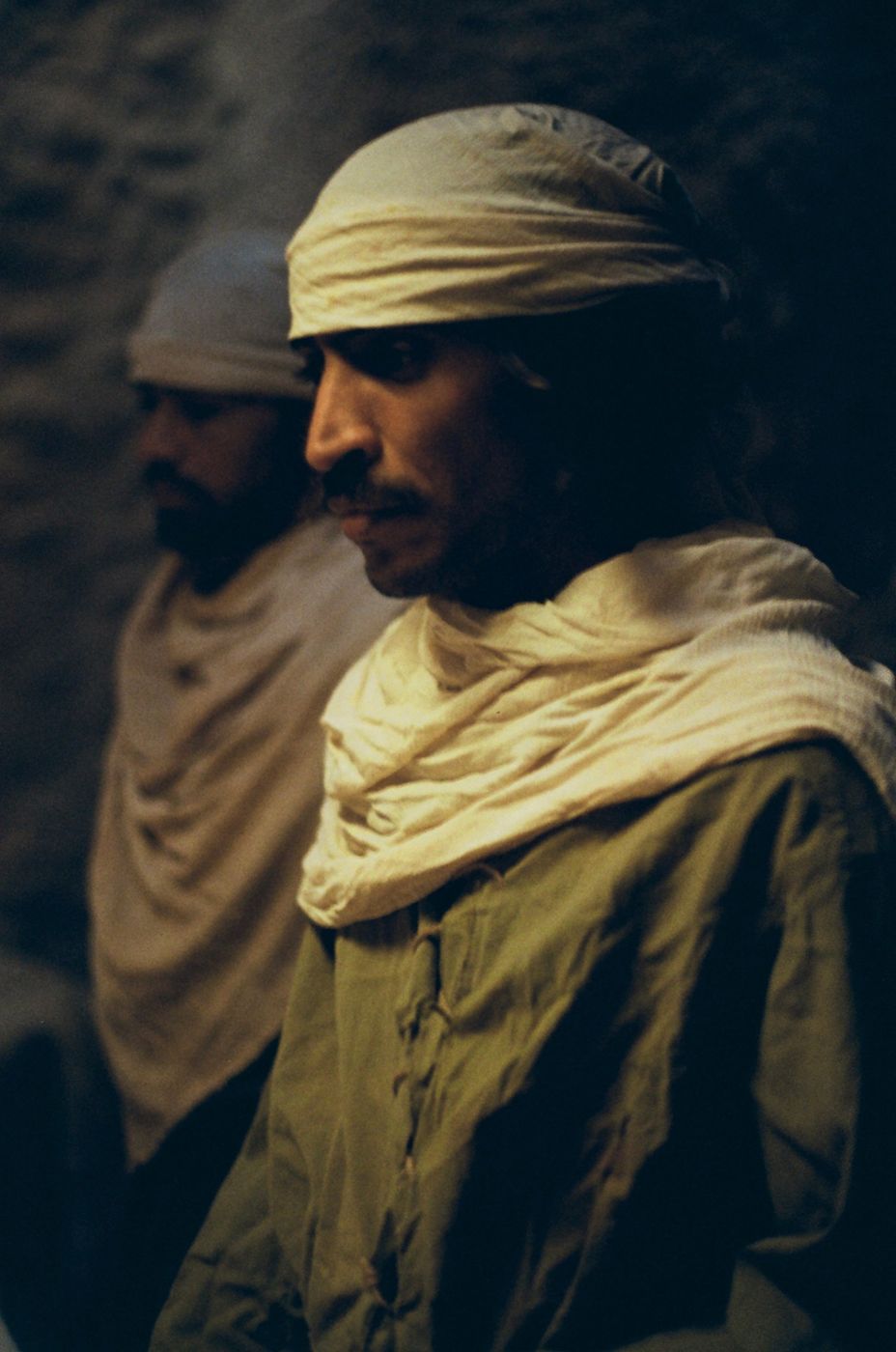 Two men in pale headwraps in low, warm light