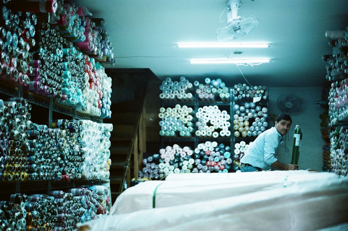 A shopkeeper among shelves of fabric rolls under fluorescent light